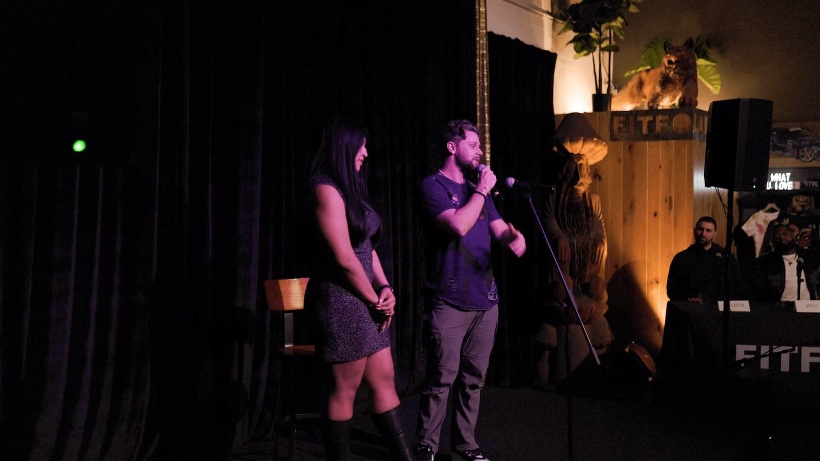 Two performers with microphones on a dark stage at a Fitfo Labs night